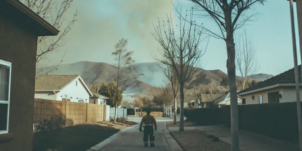 Firefighter on a suburban street assessing a wildfire hazard in the nearby hills.